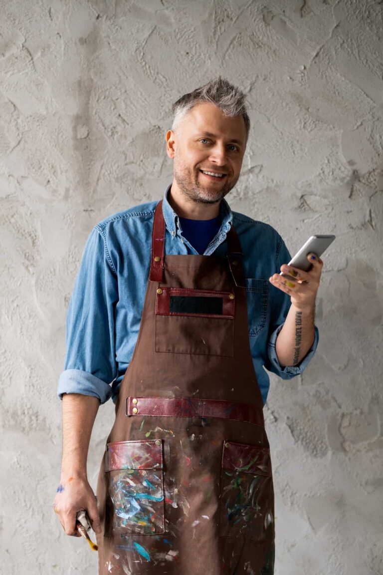 happya and successful painter with smartphone and paintbrush